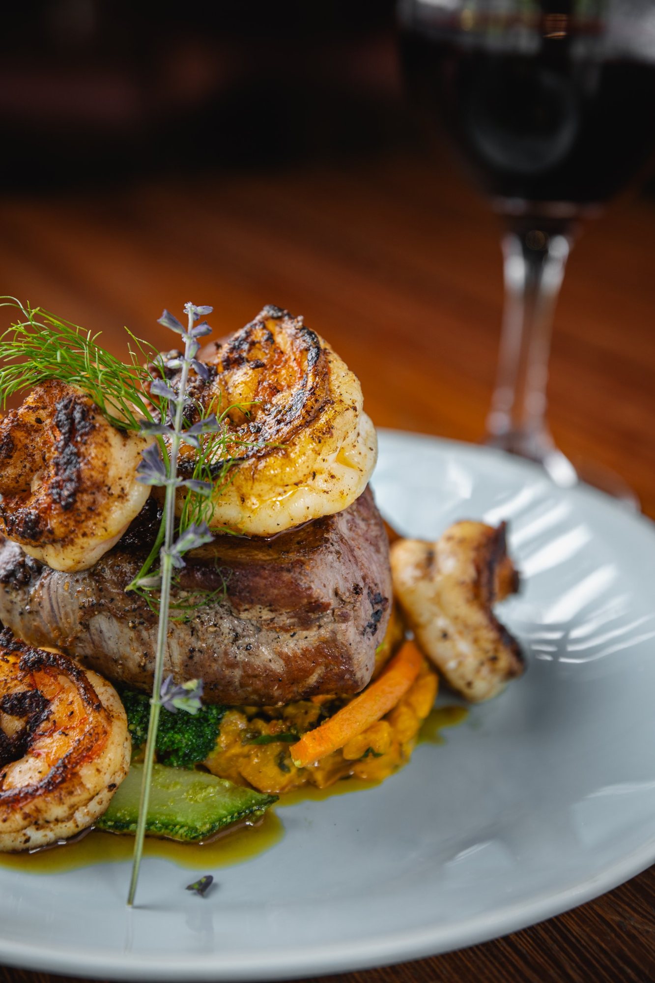 Grilled steak topped with shrimp, served with red wine